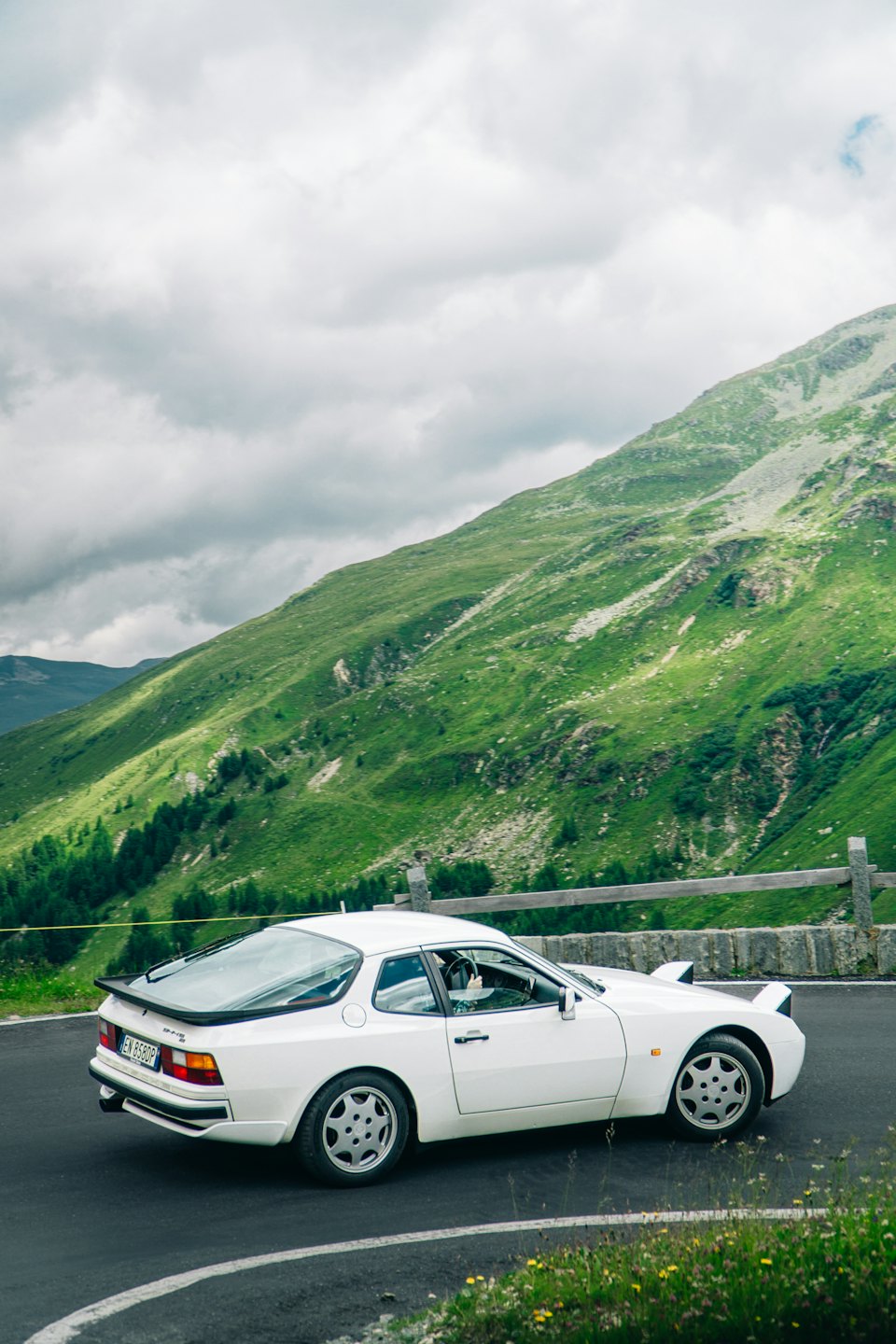 Auto sportiva bianca d'epoca parcheggiata su una strada panoramica di montagna.